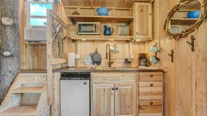 A compact kitchen with wooden cabinetry, a microwave, a sink, and a dish rack. - Mountainside Tree House Retreat (Larkspur)
