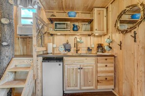 Eine kleine Küche mit Holzschränken, einer Mikrowelle, einem Spülbecken und einem Geschirrgestell.