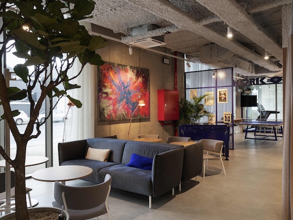 Un espace de détente moderne comprenant un canapé, des tables rondes, un buffet rouge et une table de ping-pong.