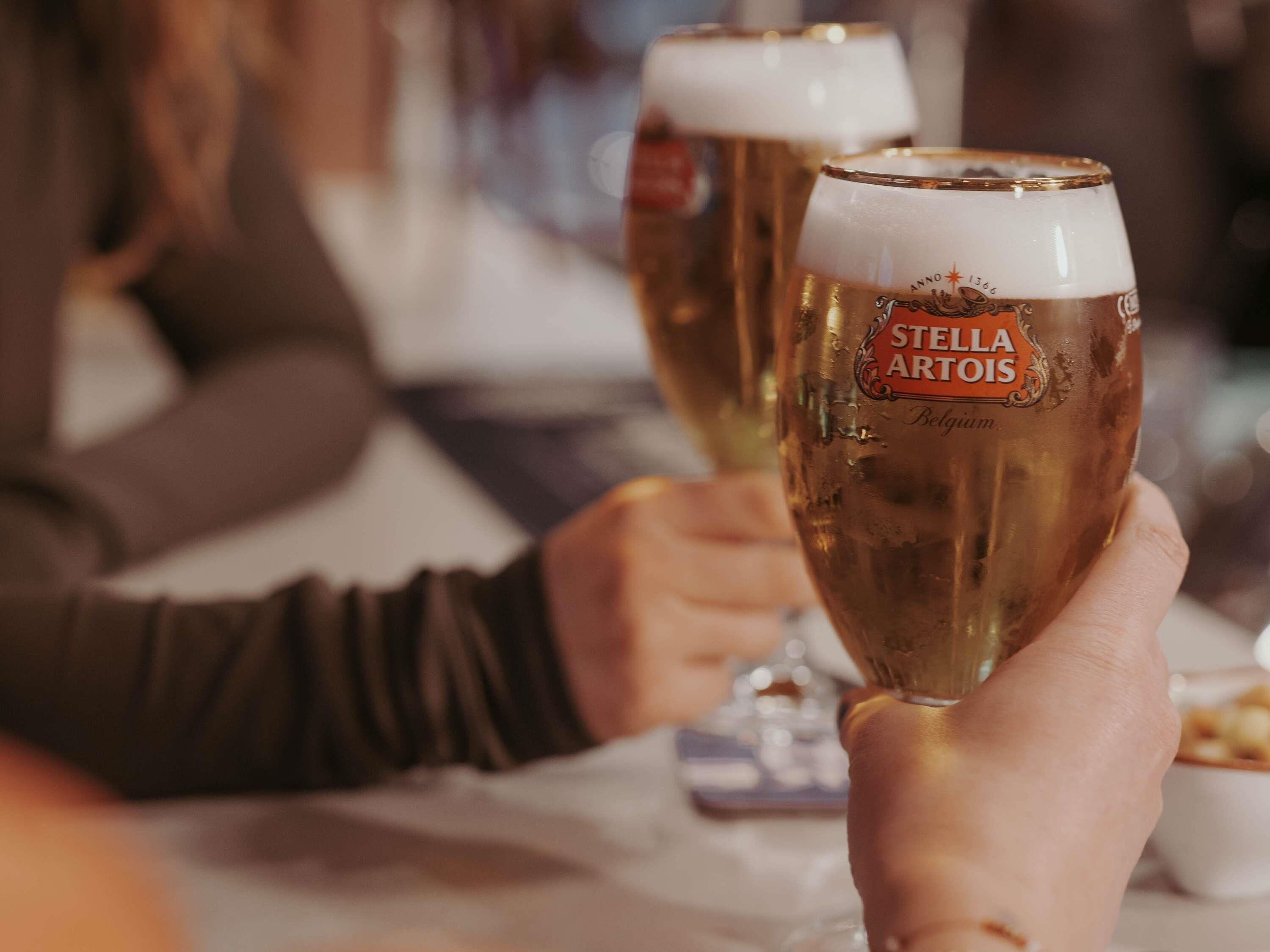 Two people holding glasses of Stella Artois beer.