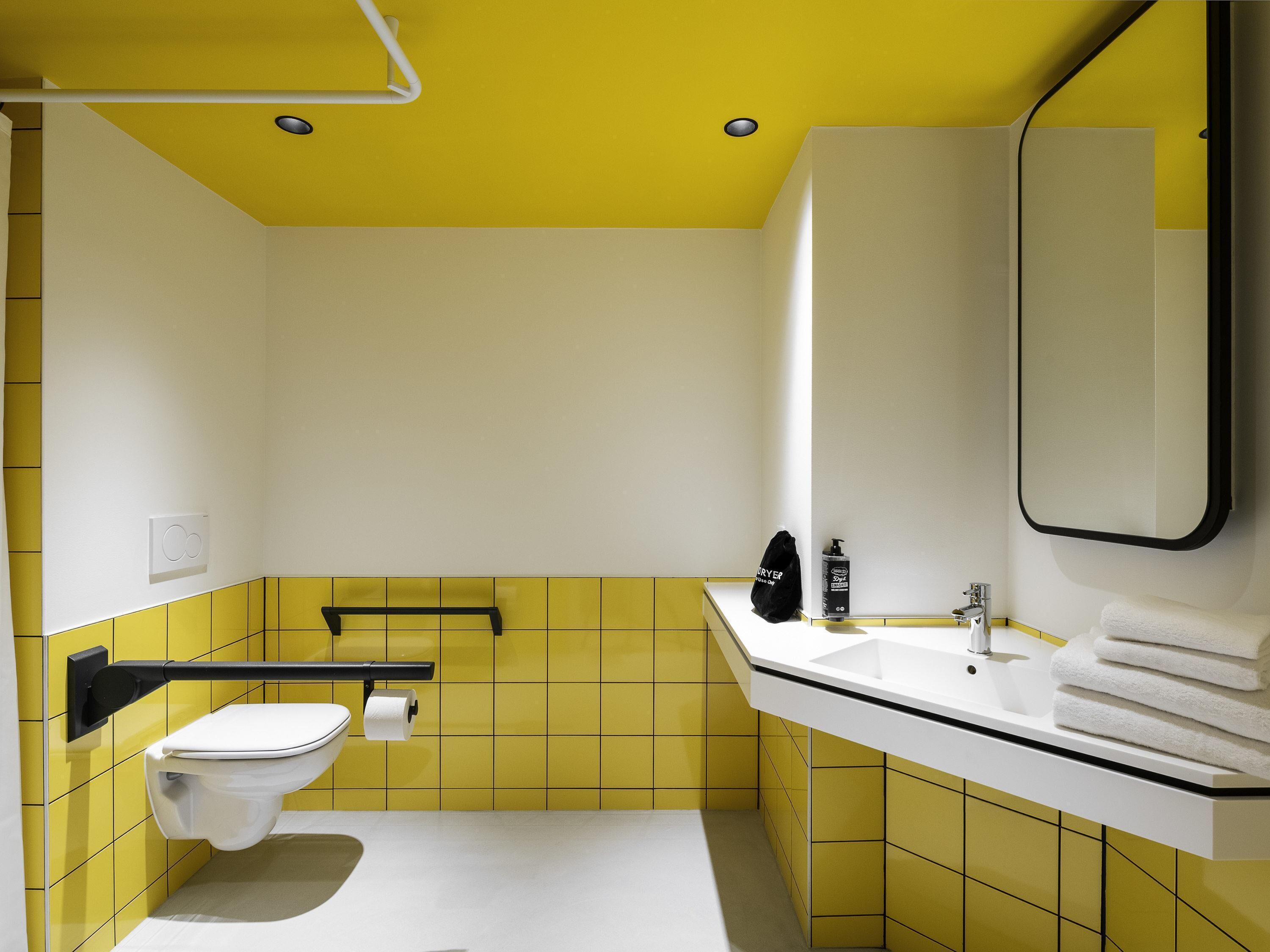 A bathroom with yellow tiles, a white toilet, a sink with a mirror, and a towel rack.