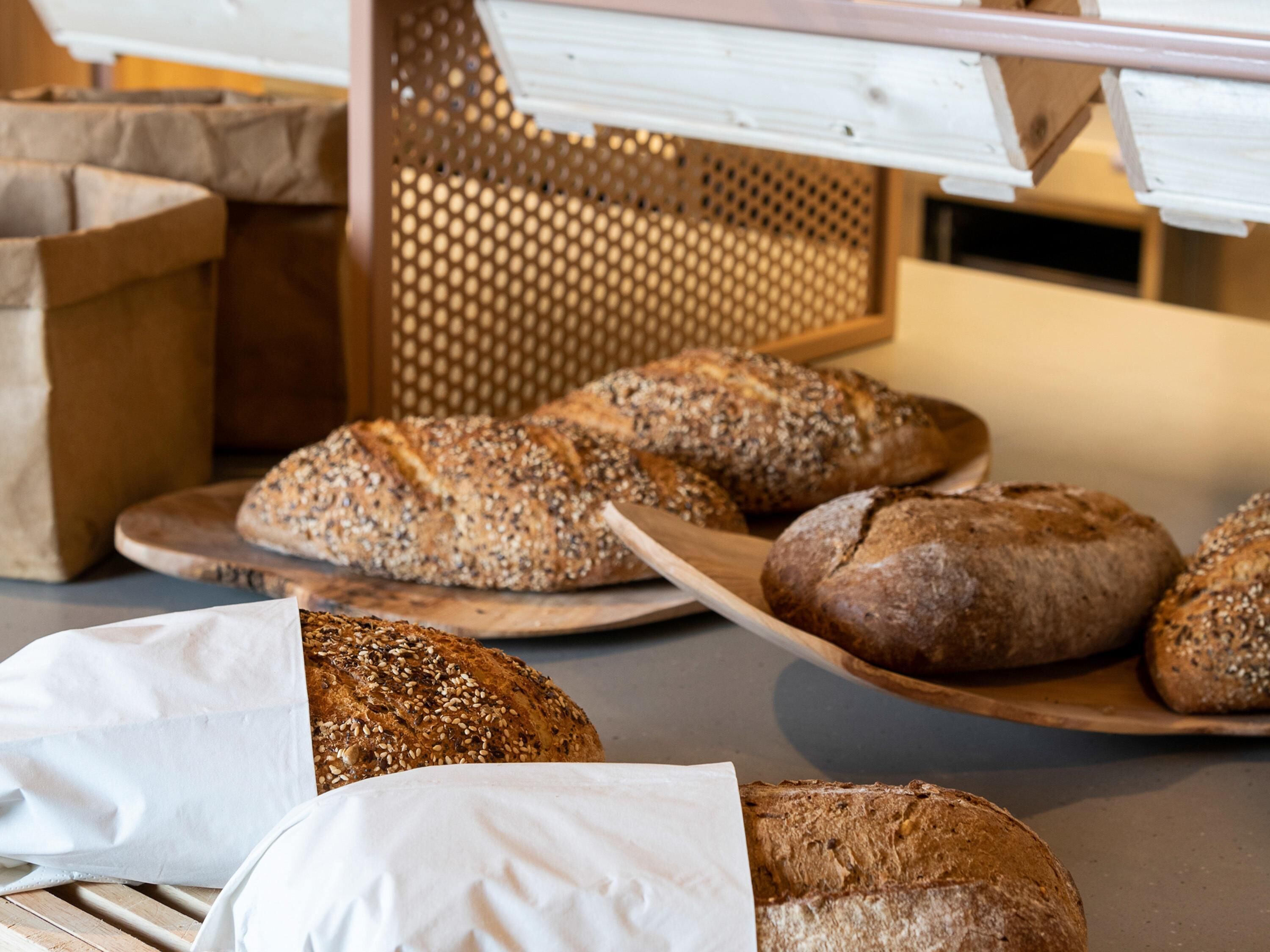 A variety of breads on wooden boards and paper bags.
