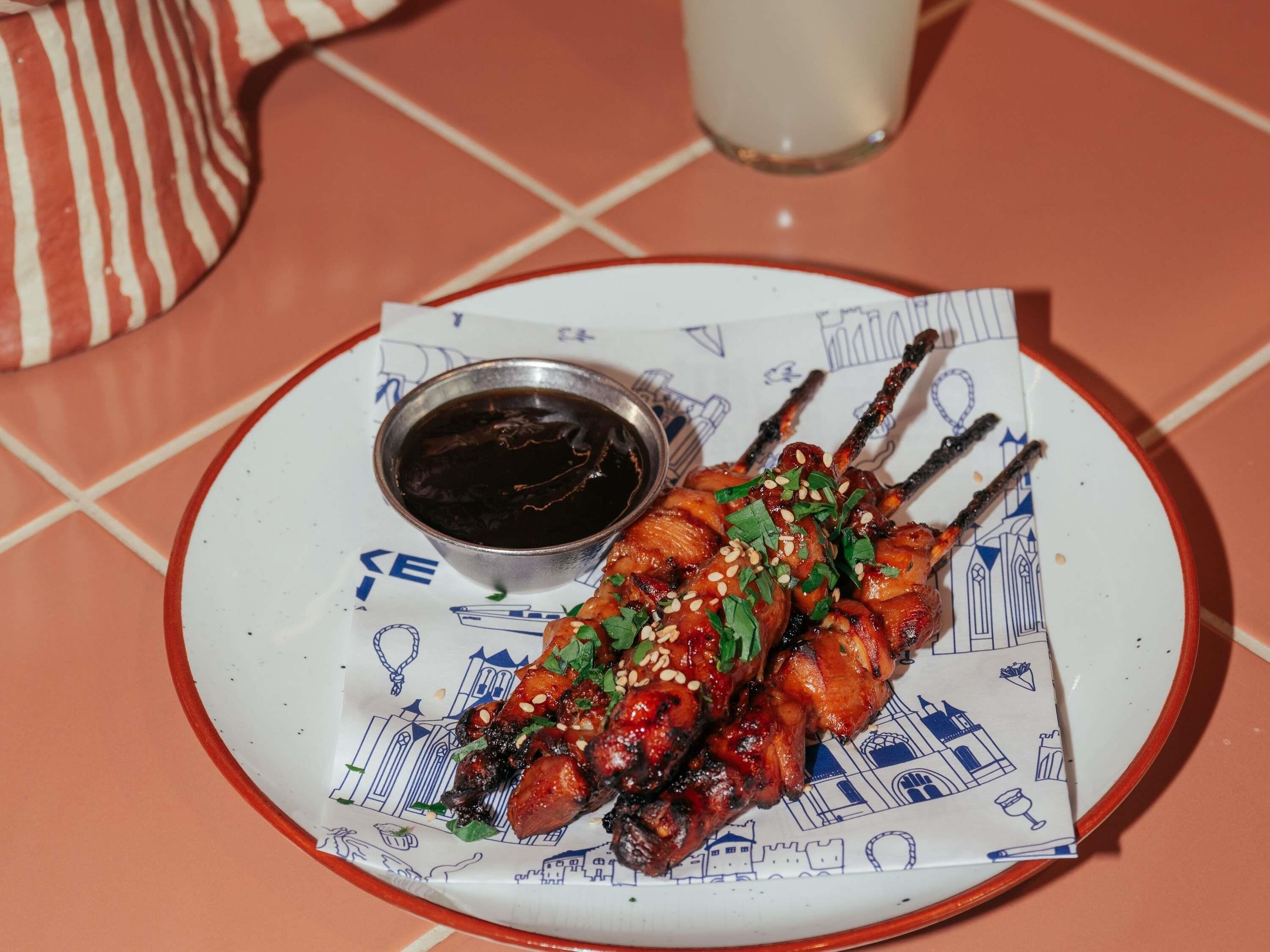 Ein Teller gegrilltes Fleisch mit einer Sauce und eine Tasse Tee auf einem Tisch mit Fliesenboden.