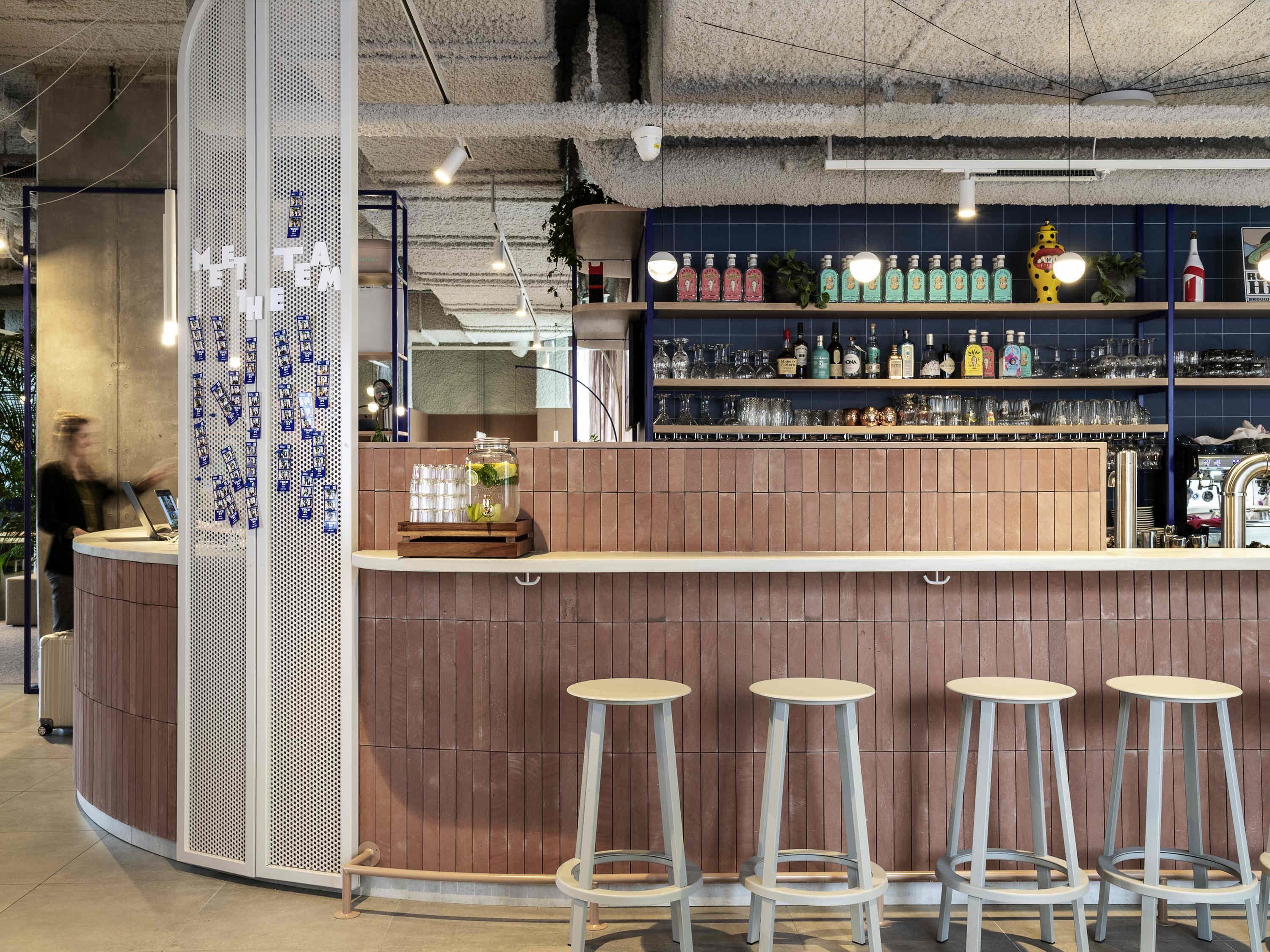 Un espace bar avec un comptoir en bois, des tabourets de bar et des étagères remplies de bouteilles et de verres.