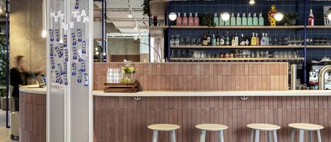 A bar area with a wooden counter, bar stools, and shelves stocked with bottles and glasses.