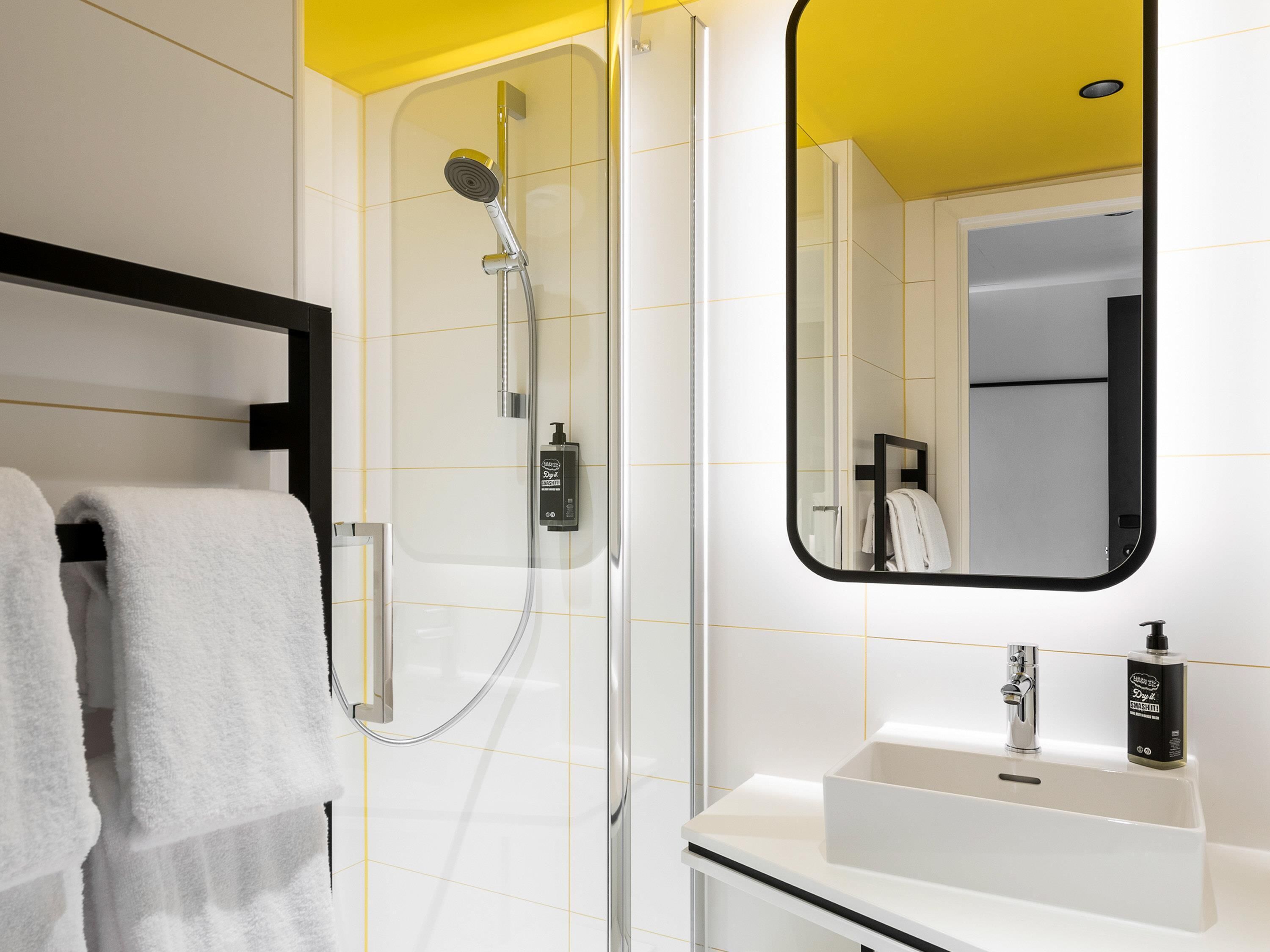 Une salle de bain moderne avec une douche à parois de verre, un lavabo blanc et un miroir avec un cadre noir.