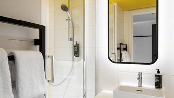 Un baño moderno con ducha de vidrio, un lavamanos blanco y un espejo con marco negro.