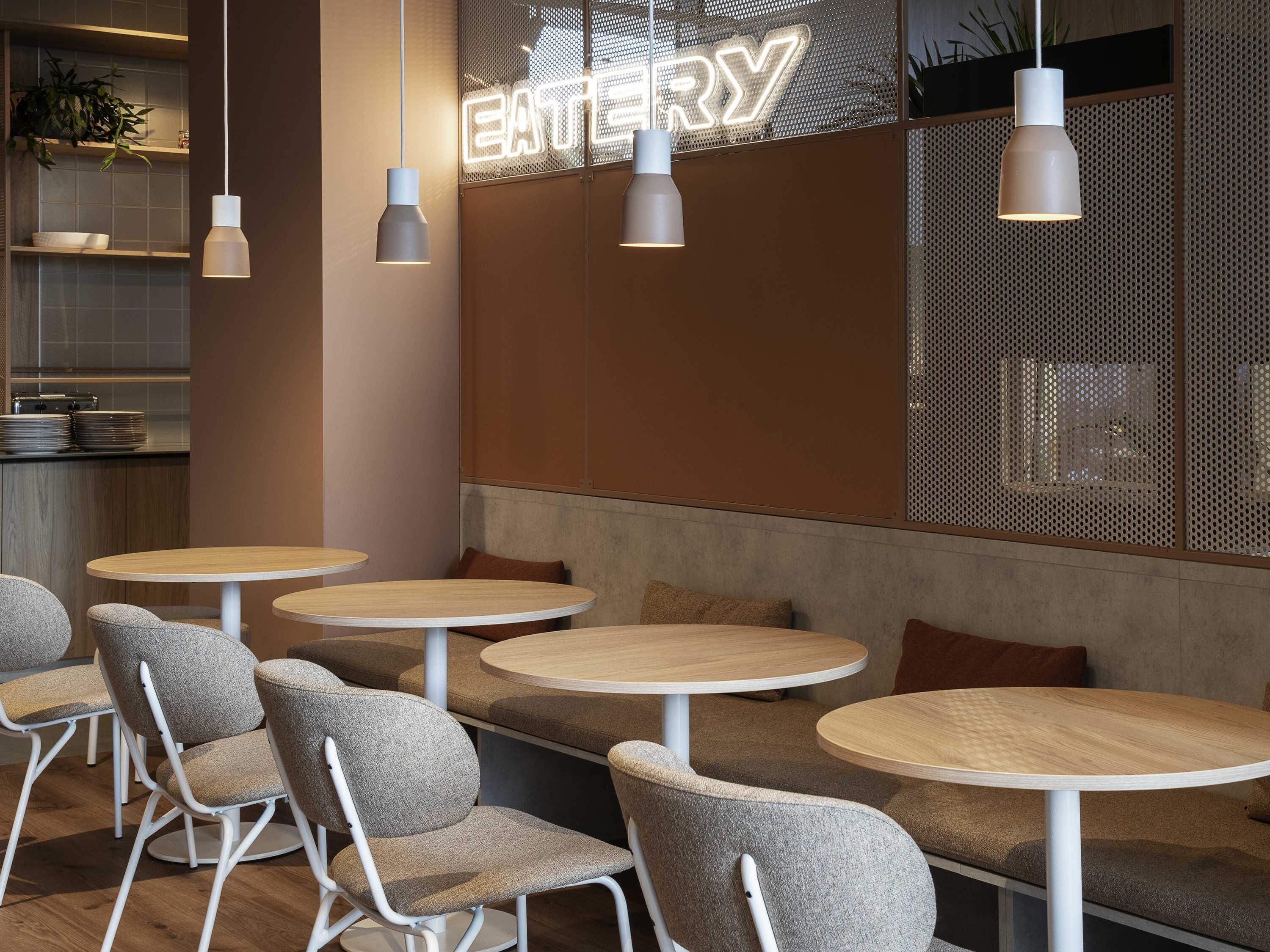 Un interior de cafetería moderno con mesas redondas, sillas tapizadas en gris y lámparas colgantes.