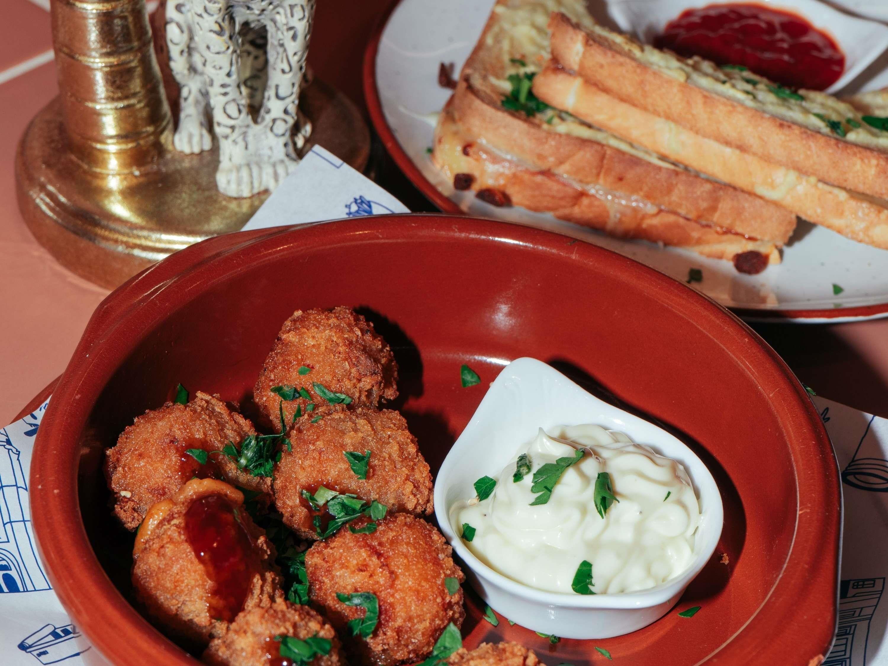 A plate of breaded and fried food with a side of sauce and a bowl of creamy dip.