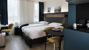A hotel room with a bed, a desk, a chair, a table with a coffee maker, and a window with curtains. - Adagio Access Gent Centrum Dampoort (Ghent)