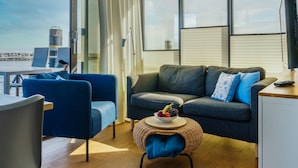 Un espace de vie moderne comprenant un canapé, des fauteuils, une petite table ronde avec des fruits, et une vue sur la mer.