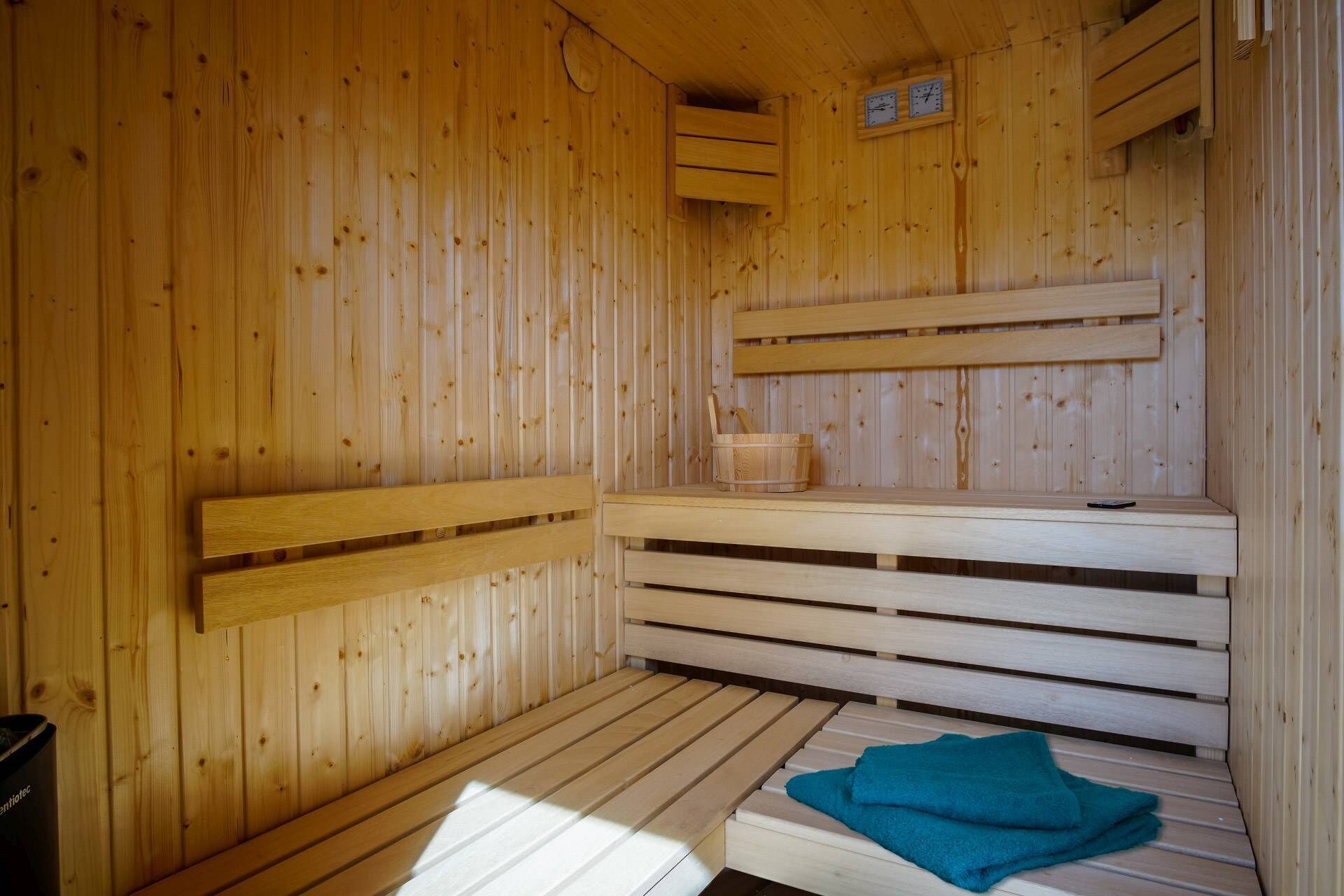Een houten sauna met banken, een zitbank en een kleine tafel met een handdoek, plus een klok aan de muur.