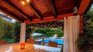 An outdoor patio with a table and chairs, a pool, and a covered area with a wooden ceiling and hanging plants. - Large outdoor with privacy, Heated pool 60m2 , Gamesroom ,Wellness, Garden (Karojba)
