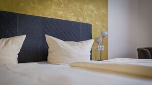 A neatly made bed with white linens and two pillows, a dark headboard, and a wall with a textured golden finish. - Gasthaus Mohren (Pfullendorf)