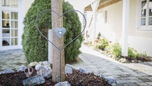 A heart-shaped metal decoration on a tree in a garden area with a paved walkway and a building in the background. - Gasthaus Mohren (Pfullendorf)