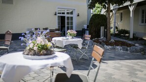 An outdoor patio area with tables and chairs, a potted plant, and a building entrance. - Gasthaus Mohren (Pfullendorf)