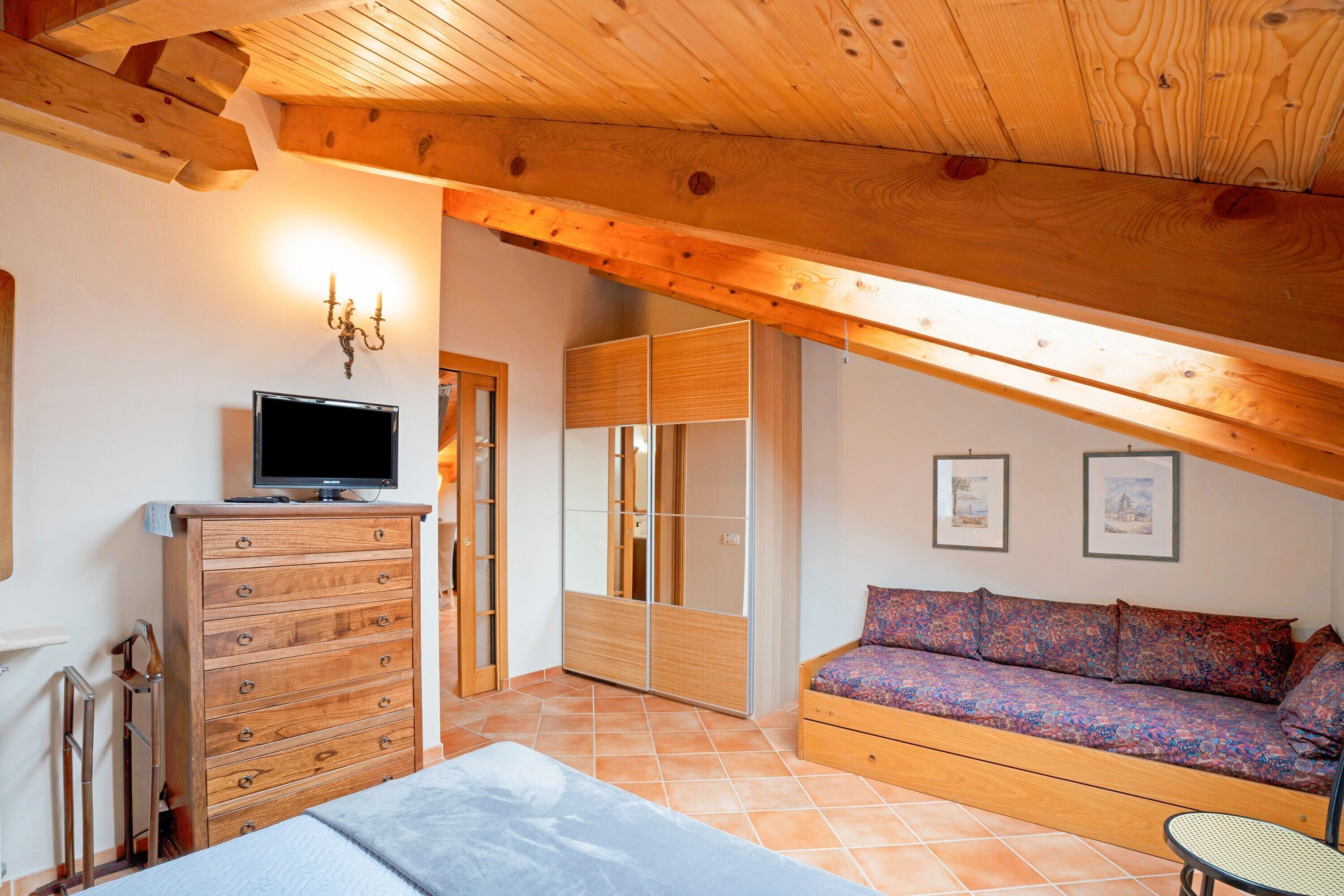 Une chambre avec un plafond en bois, une commode, un téléviseur, un canapé et un lit.
