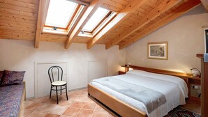 Ein Schlafzimmer mit Holzboden, Dachfenstern, einem Bett, einem Sessel und einem Nachttisch.