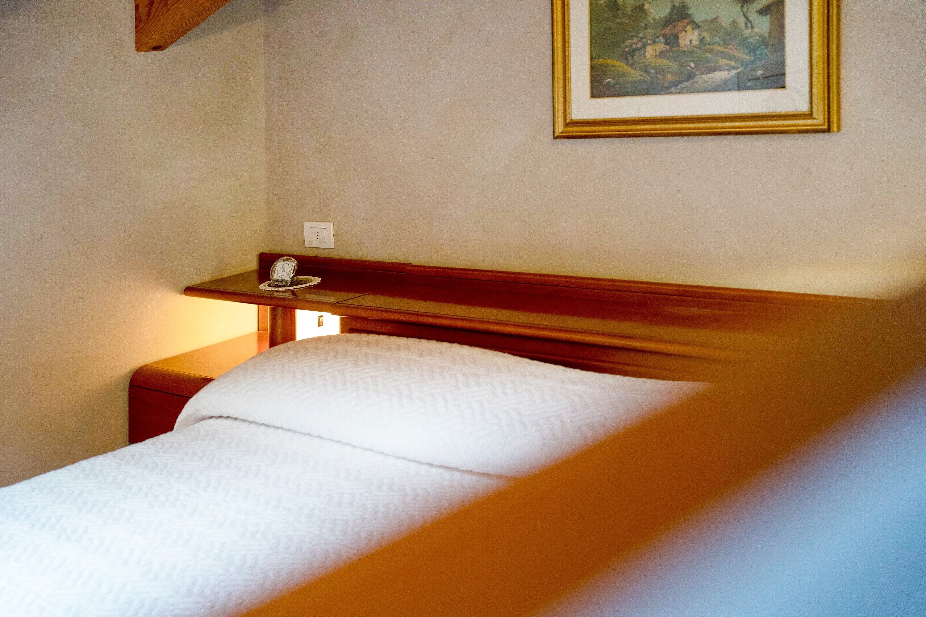 Ein Einzelbett mit Holz-Kopfteil, ein Nachttisch mit Lampe und ein gerahmtes Bild an der Wand.