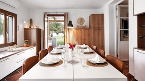 Een eethoek met een witte tafel voor vier personen, houten kasten en uitzicht op het omliggende landschap.