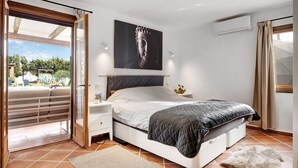 Een slaapkamer met een bed, nachtkastje, wandairconditioner, raam met gordijnen en uitzicht op de omgeving.