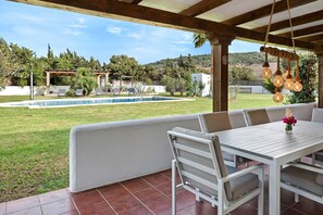 A covered patio with a pool, outdoor seating, and a view of the surrounding landscape.