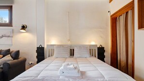 Siististi pedattu sänky, jossa on tyynyjä, yöpöydällä lamppu ja lattialla matkalaukku.