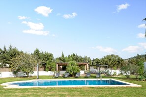 A swimming pool with lounge chairs, a pergola, and a garden with trees and shrubs. - Villa la Luna La Casita – Loft with Shared Pool & Terrace in Vejer, Cádiz (VEJER DE LA FRONTERA)