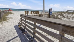 A wooden boardwalk leading to a beach with a safety sign and a wooden structure in the background. - Beachside Villas #413 | Pet-Friendly Condo, Near Beach with Pool (Seagrove Beach)