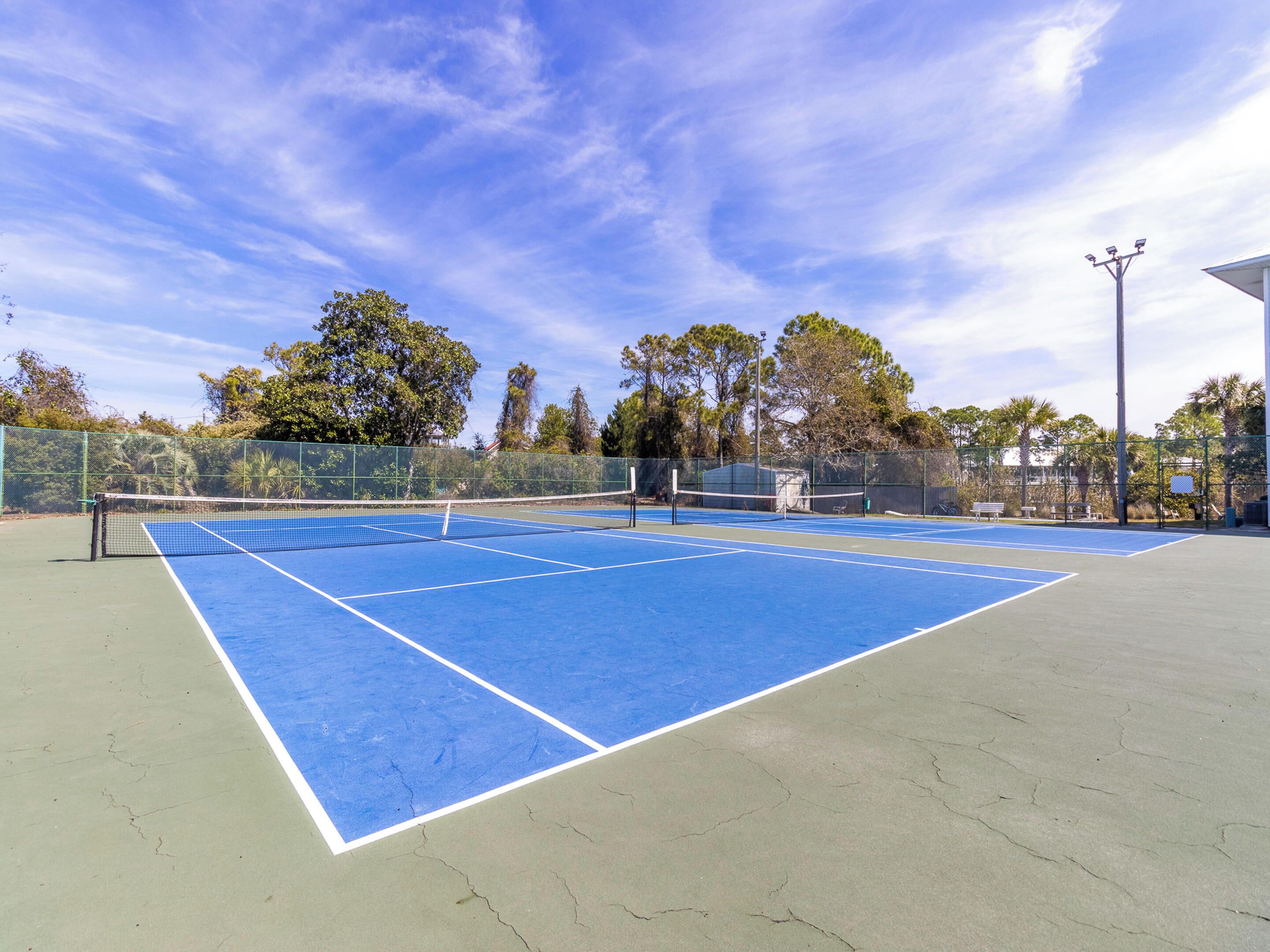 A tennis court with a net, surrounded by trees and a fence.