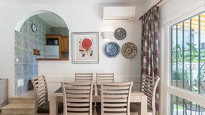 Een eethoek met een tafel en stoelen, een keuken op de achtergrond, decoratieve borden en een airconditioner.