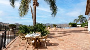 Une terrasse avec une table et des chaises, un palmier, une piscine et une vue sur les montagnes.