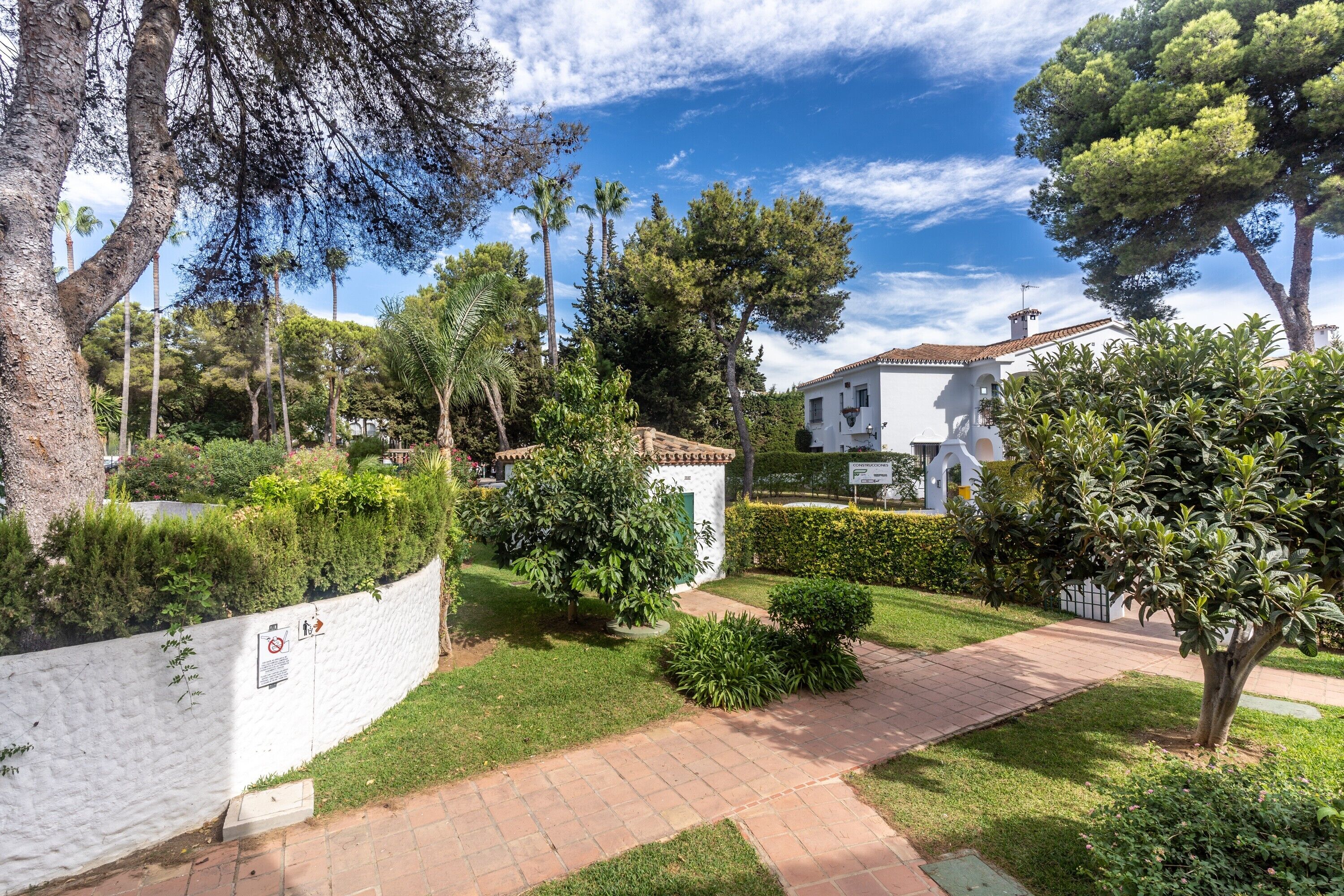 Un barrio residencial con un edificio blanco, un sendero pavimentado y varios árboles.