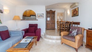 Ein Wohnzimmer mit einer Couch, einem Sessel und einem Couchtisch, ein Essbereich mit Stühlen und eine Küche mit Schränken und einem Esstisch.