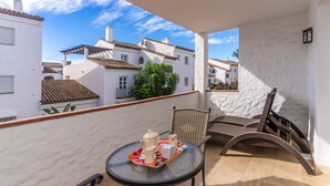 Ein Balkon mit Tisch, der für Tee gedeckt ist, Korbstühle und Blick auf weiße Gebäude mit Ziegeldächern.