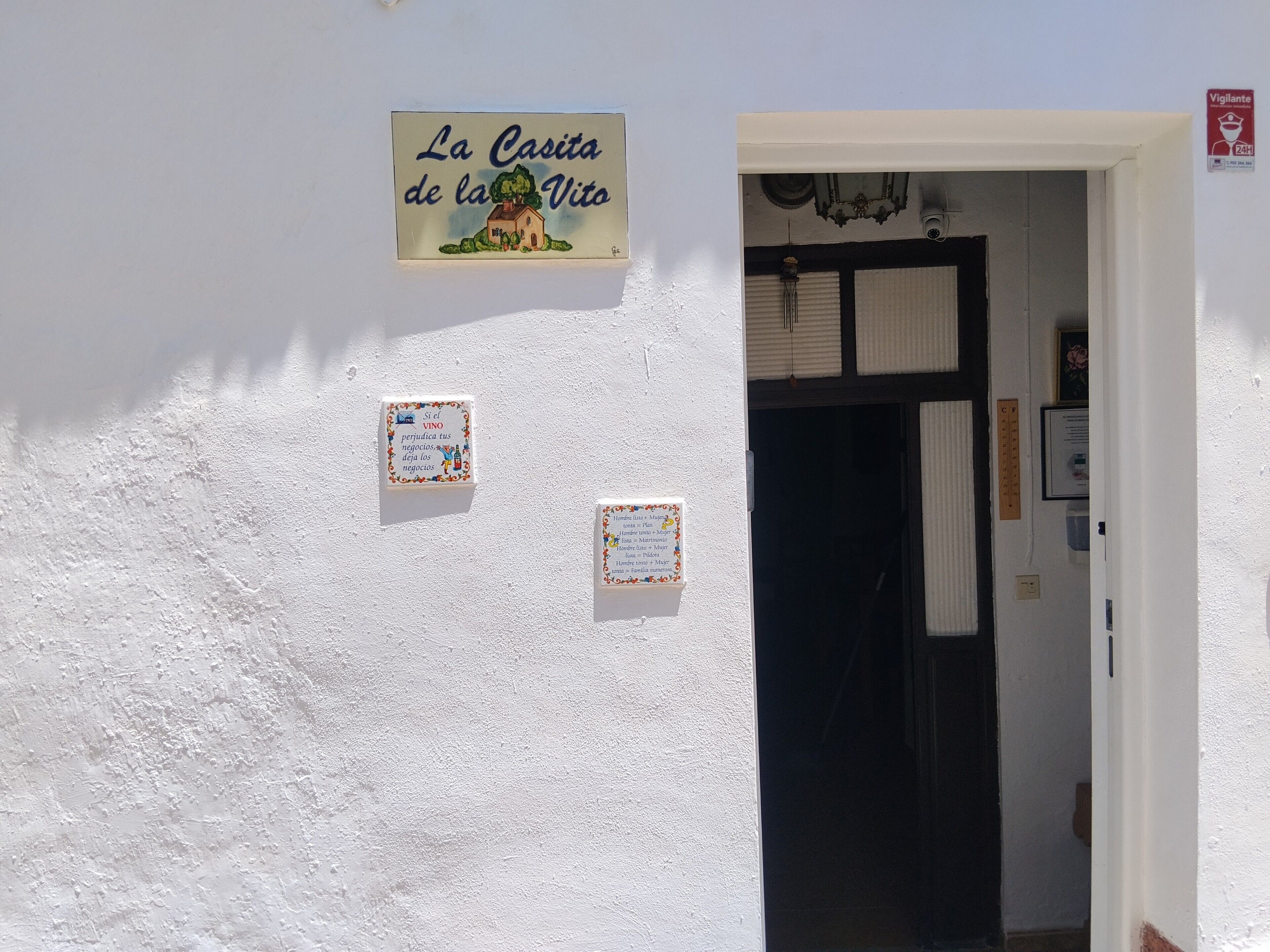Una pared blanca con un letrero que dice 'La Casita de la Voto' y dos letreros más pequeños debajo.