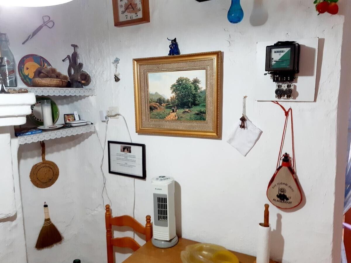 A room with a white wall, a framed picture, a small heater, a chair, and a shelf with various items.