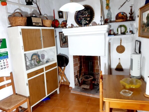 Une pièce avec une cheminée, un meuble en bois, une table sur laquelle se trouve un bol jaune, et divers objets décoratifs disposés sur des étagères.