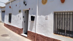 Un bâtiment blanc avec une base marron, une porte, une fenêtre avec un grillage métallique et une petite enseigne sur le mur.