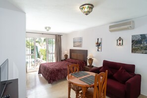 Une chambre d’hôtel comprenant un lit, un canapé, une table à manger avec des chaises, un téléviseur et une fenêtre avec des rideaux.
