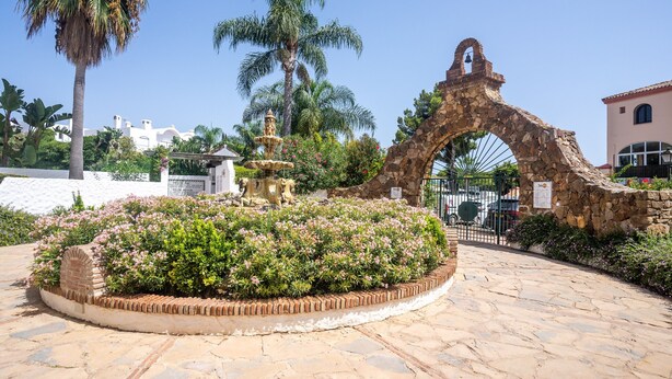 A stone archway, a fountain, and a circular flower bed with a brick border. - Studio Apartment '19A Claire' with Pool, Private Garden & Wi-Fi (El Paraiso)