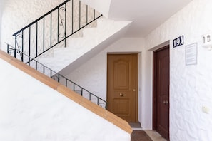 Una escalera con barandilla de madera y balaustradas de metal negro, una puerta de madera y un cartel fijado a la pared con el número '19A'.