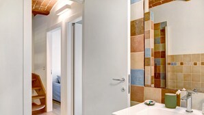 Un baño con salpicadero de azulejos, un lavamanos, un espejo y una puerta de madera que da a un dormitorio.