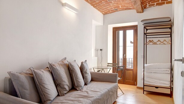 Una habitación con sofá, cama, mesa y puerta que da a un balcón exterior.