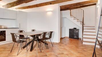 A dining area with a wooden table and chairs, a kitchen with white cabinets, and a staircase leading to an upper level.
