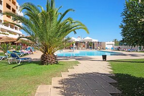 A pool area with lounge chairs, a palm tree, and a building in the background. - Studio "Belavista House" with Private Terrace, Shared Pool & Wi-Fi (Albufeira)