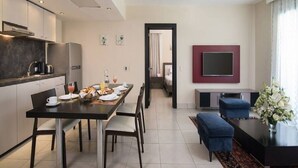 A modern hotel room with a dining area, a living area with a TV, and a kitchen with a refrigerator and coffee maker. - Luxurious 1 Bedroom Royal Suite (Dominican Republic)
