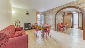 Un salon avec un canapé, une table à manger, des chaises, un téléviseur et un mur en pierre.