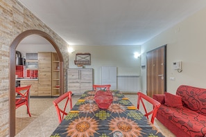 Un coin repas avec une table dressée pour quatre personnes, un canapé rouge et une cuisine en arrière-plan.