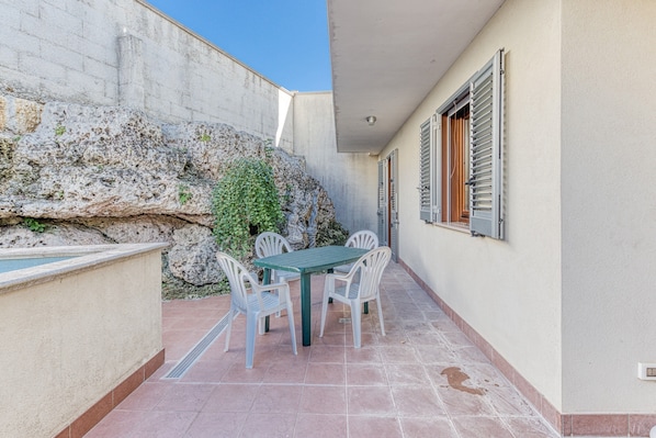 Une terrasse avec une table et des chaises, un mur en pierre et une fenêtre avec des volets.